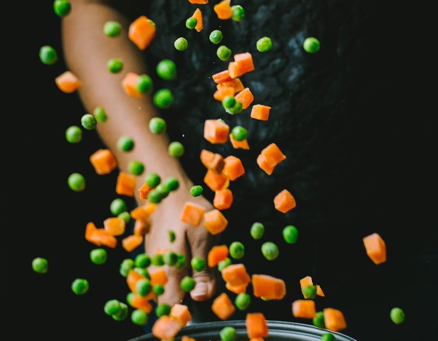 Frozen peas and diced carrots falling against a dark background